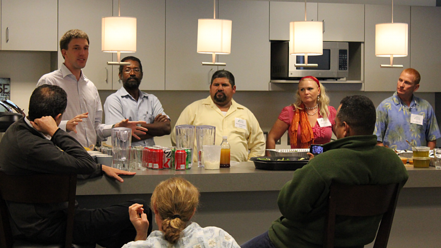 One mean speaking to a group of people gathered around a table