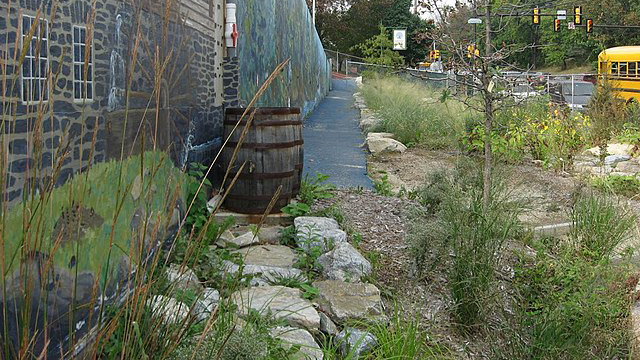 A rain barrel standing outside the wall of a building