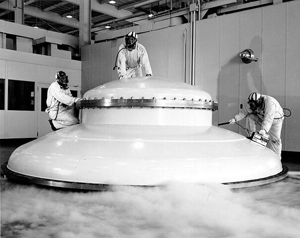 A black and white photo of three people in spacesuits climbing on an object that looks like a spaceship