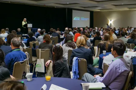 People seated at tables listening to a speaker at the symposium